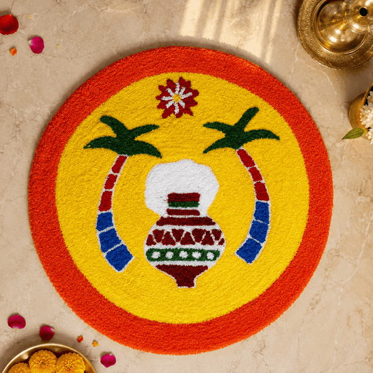 A round tufted rug with a bright yellow center, red-orange border, and embroidered motifs including a white pot, green leaves, and red and blue curved accents, displayed on a beige marble surface with decorative props.
